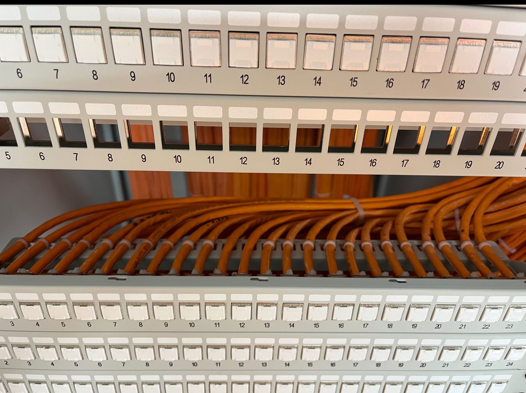 Panel krosowniczy z pomarańczowymi kablami sieciowymi, widoczne numery portów. Instalacja okablowania strukturalnego w serwerowni lub szafie telekomunikacyjnej.