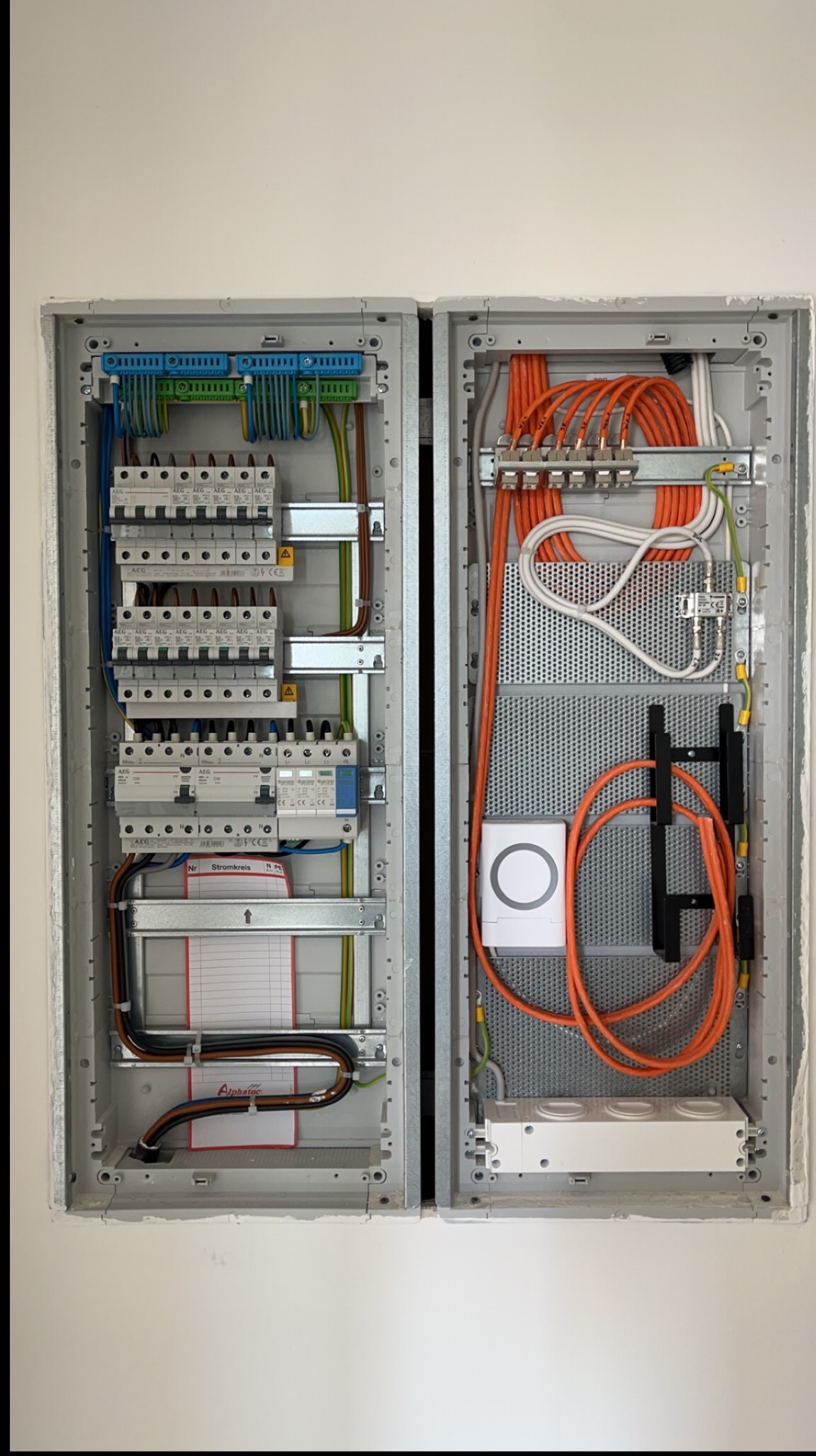 Rozdzielnica elektryczna z bezpiecznikami, przewodami i elementami automatyki, zamontowana w ścianie. Widoczne szczegóły instalacji i podłączeń.