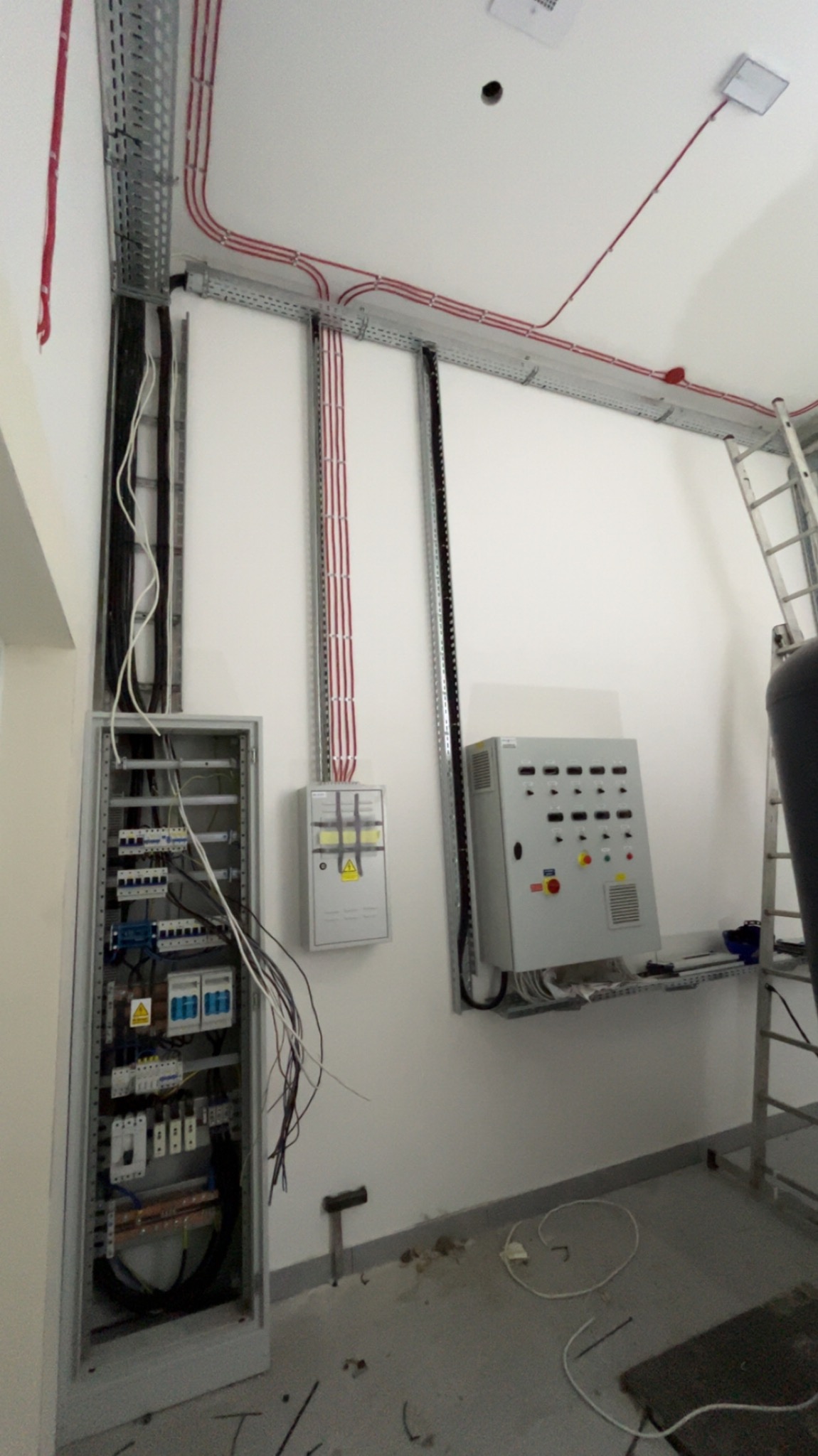 Rozdzielnica elektryczna z przewodami w korytkach i peszlach na ścianie. Widoczne zabezpieczenia i aparatura. Instalacja w nowym budynku.