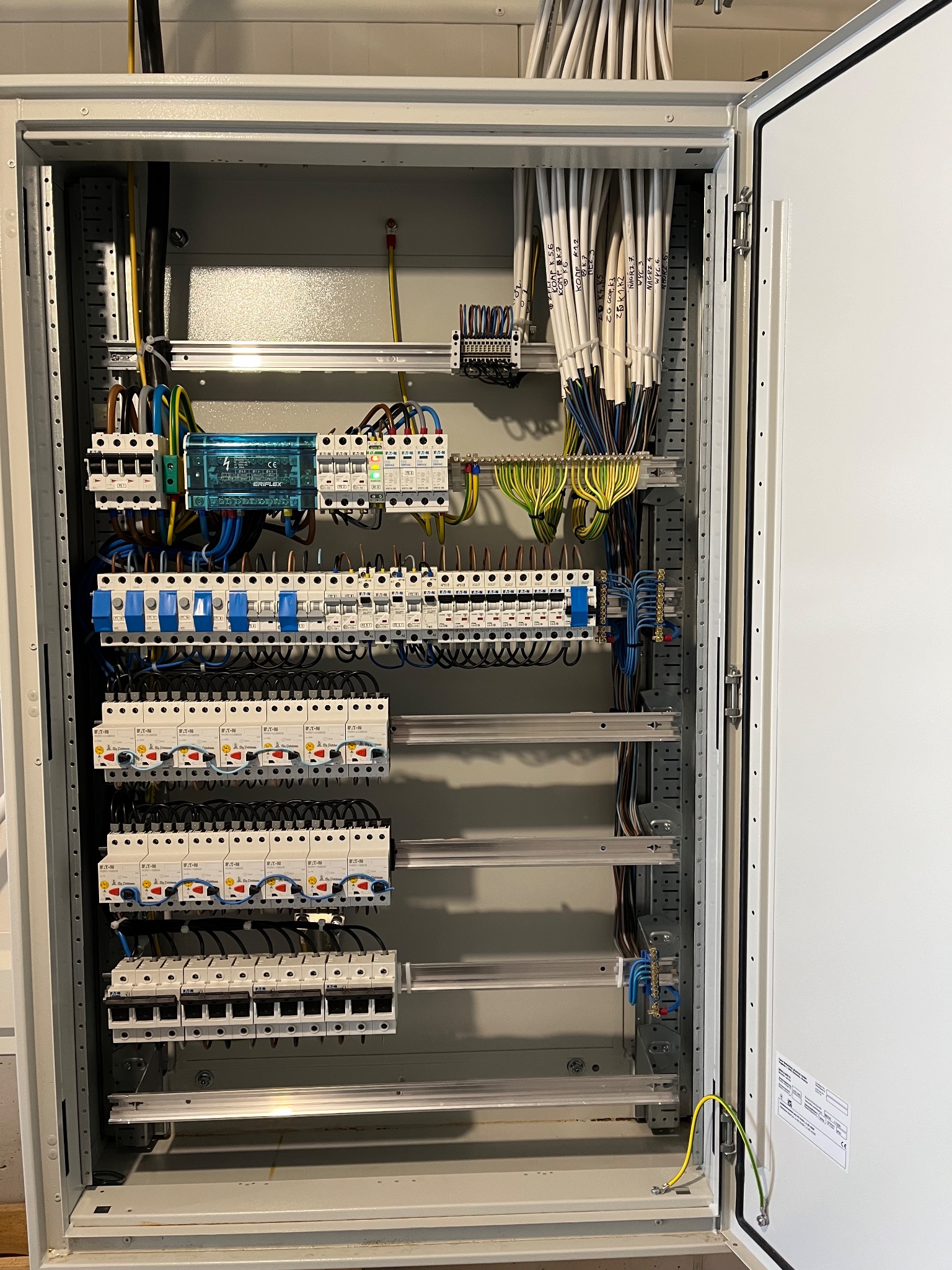 Rozdzielnica elektryczna z zainstalowanymi bezpiecznikami, przewodami oznaczonymi etykietami i elementami montażowymi. Widoczne detale instalacji i staranne ułożenie kabli.