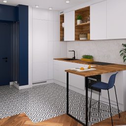 Wnętrze z sensem - Wnętrze nowoczesnej kuchni z białymi szafkami, drewnianym blatem i niebieskimi akcentami. Widoczny stół barowy z krzesłem i fragment sofy.