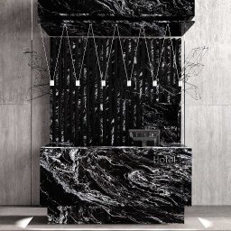 Archistone Wojciech Dodzian - Recepcja hotelowa z blatem z czarnego kamienia o unikalnym wzorze żyłkowania, podświetlona minimalistycznymi lampami. Tło stanowi betonowa ściana.