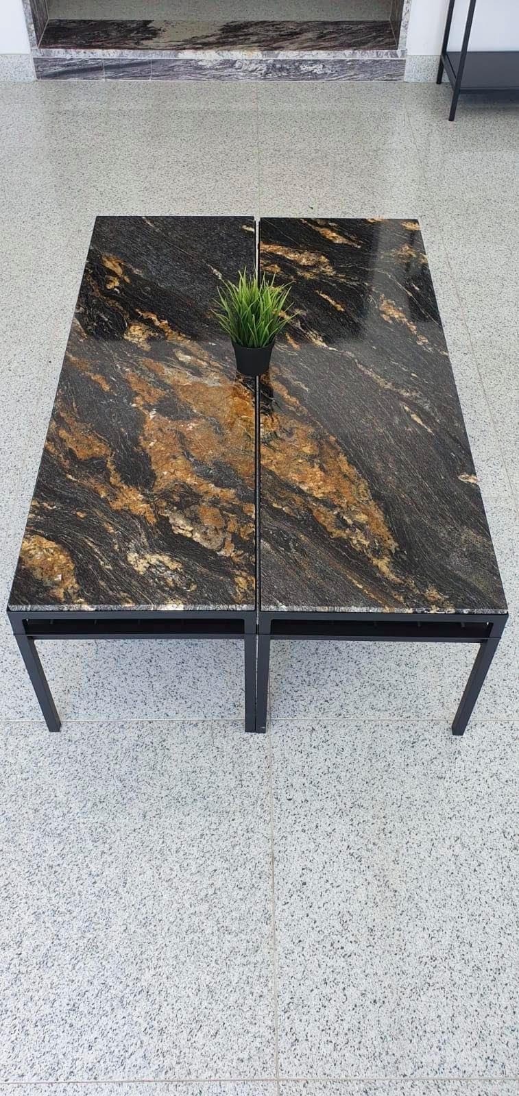 Dwa stoliki kawowe z blatem z czarnego, polerowanego kamienia z brązowymi żyłkami, na metalowych nogach. Na stolikach stoi mała roślina doniczkowa.