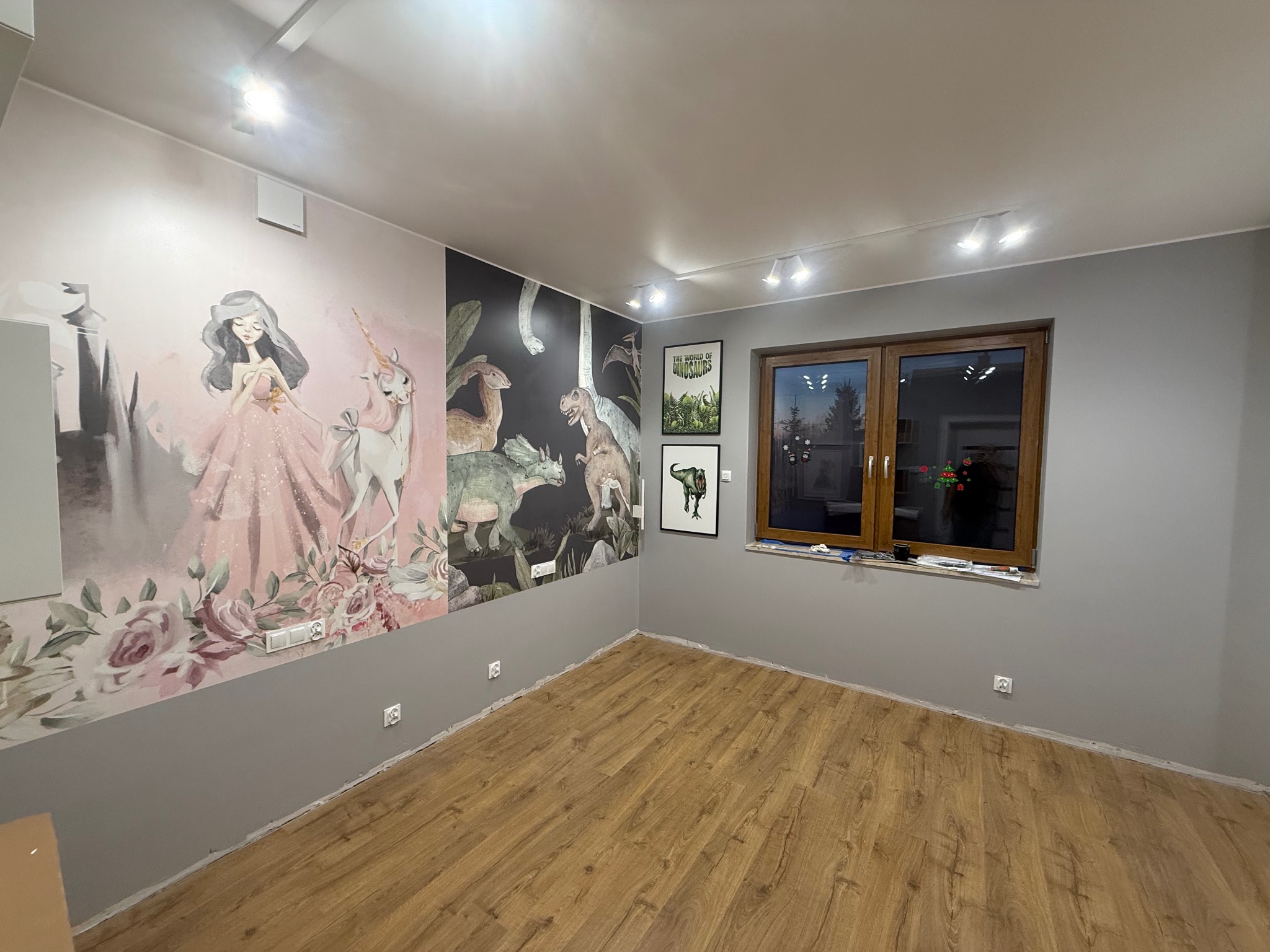 Pokój dziecięcy po malowaniu ścian z motywami bajkowymi i dinozaurami. Na podłodze panele. Okno z drewnianą ramą. Oświetlenie sufitowe.