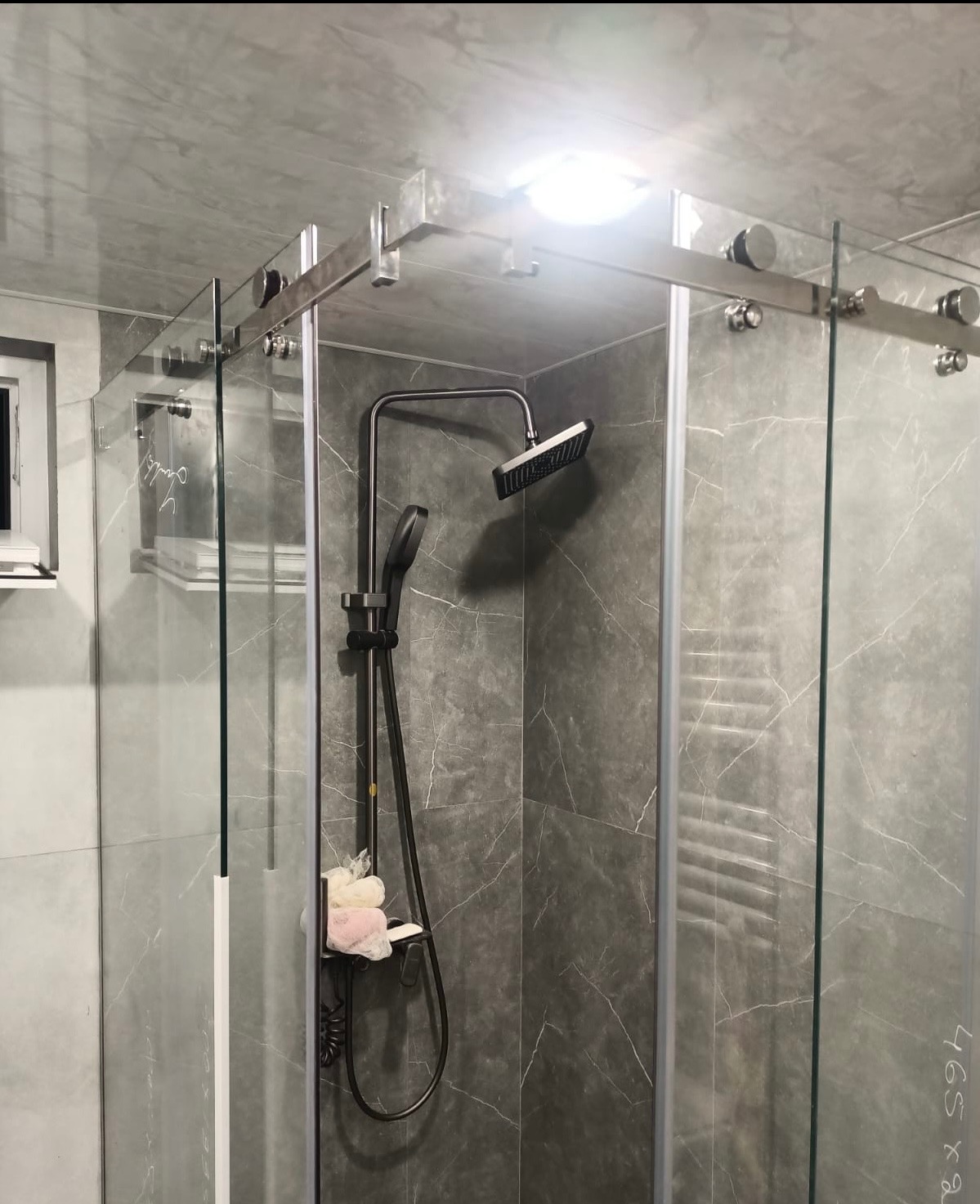 Szklana kabina prysznicowa z deszczownicą i półką na akcesoria, wykończona płytkami imitującymi marmur. Nowoczesny design, chromowane elementy.