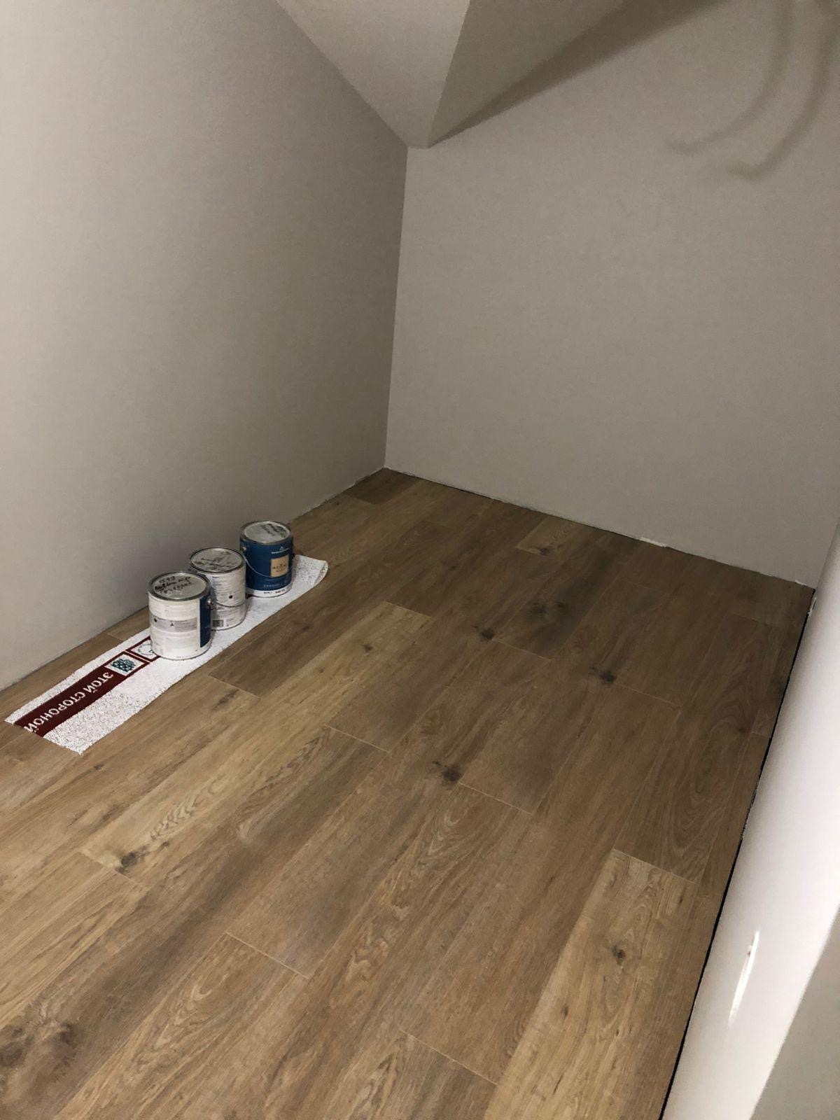 Przygotowania do malowania: trzy puszki z farbą stoją na podkładce na drewnianej podłodze w rogu pokoju z pomalowanymi na szaro ścianami. Widok z góry.