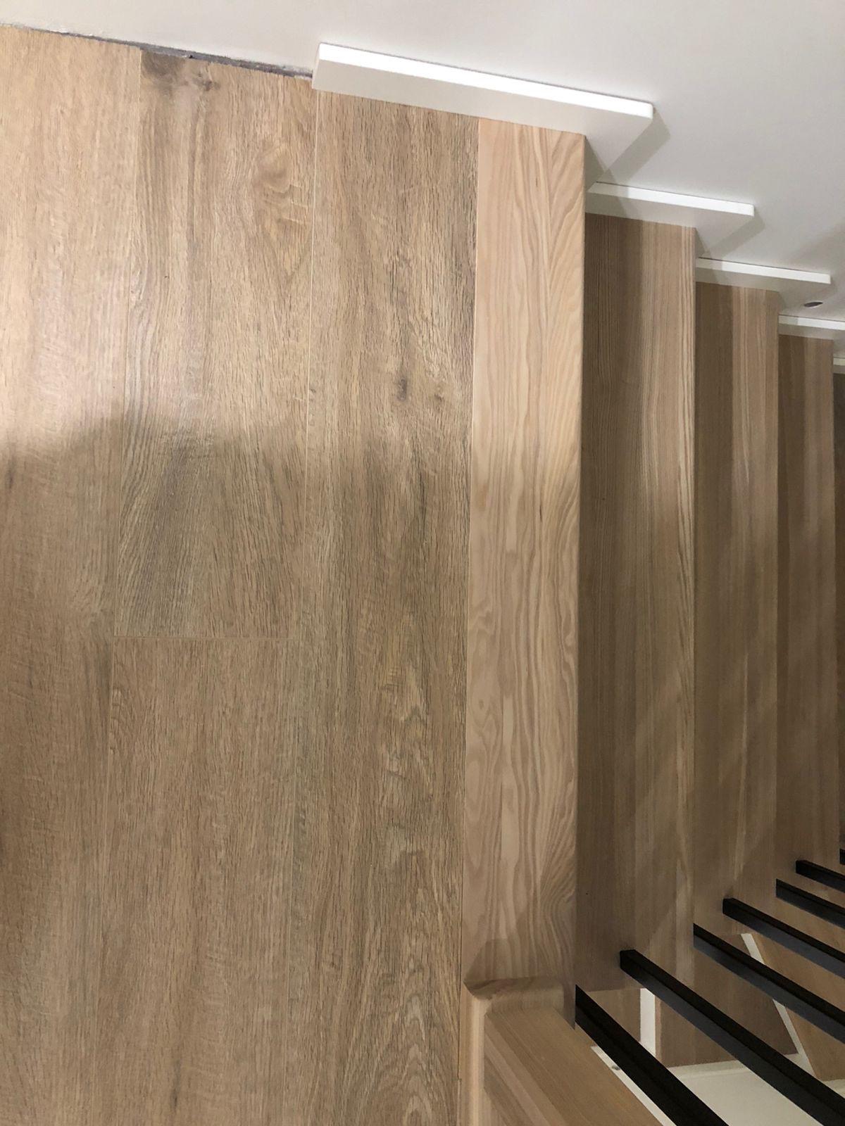 Wykończone schody z drewnianymi panelami ściennymi w odcieniach beżu i brązu, z czarnymi elementami konstrukcyjnymi. Nowoczesny design z dbałością o detale.