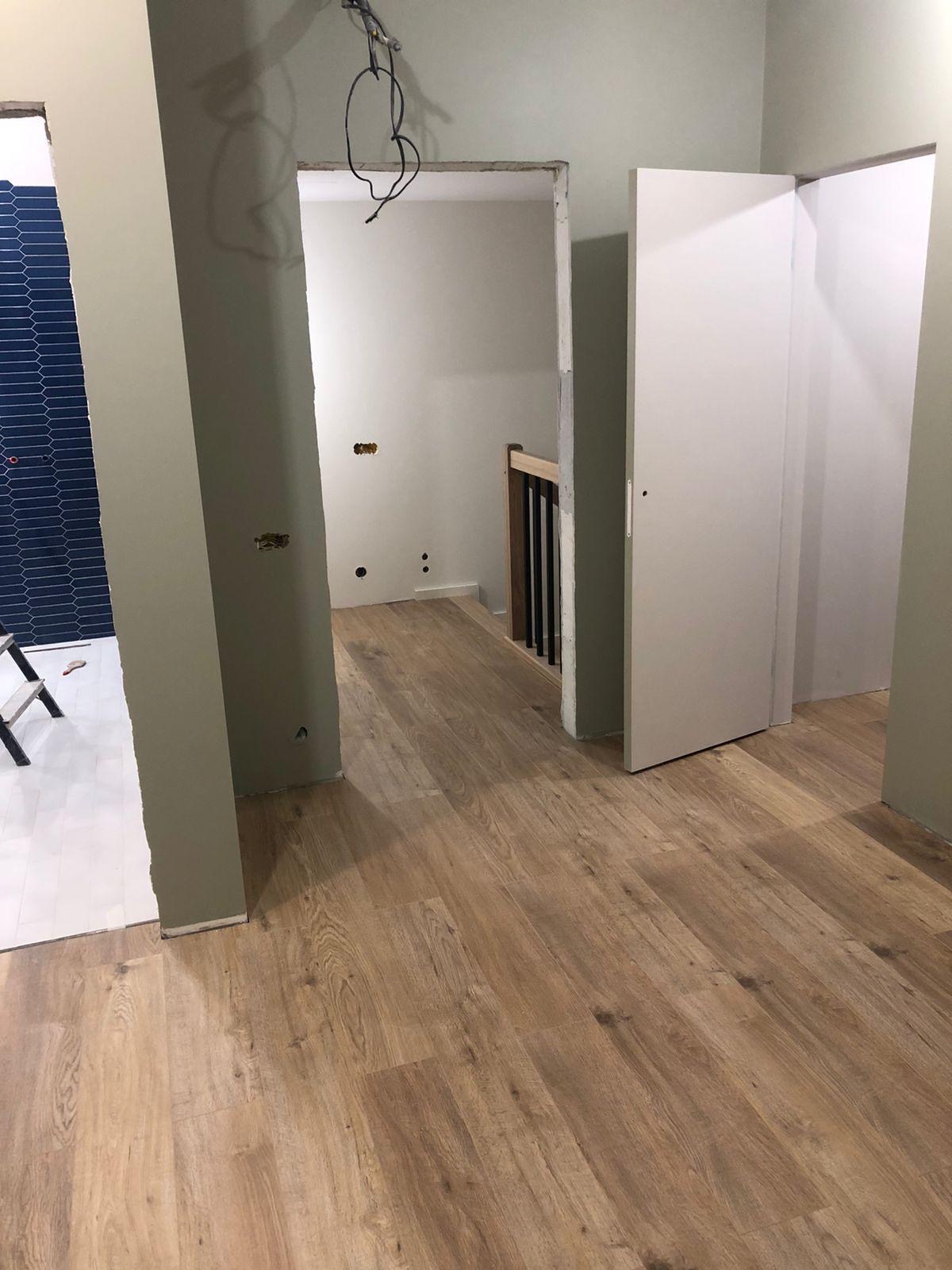 Wnętrze w trakcie prac wykończeniowych: położona podłoga, częściowo wykończona łazienka z niebieską glazurą, widoczne kable i przygotowane otwory na gniazdka.