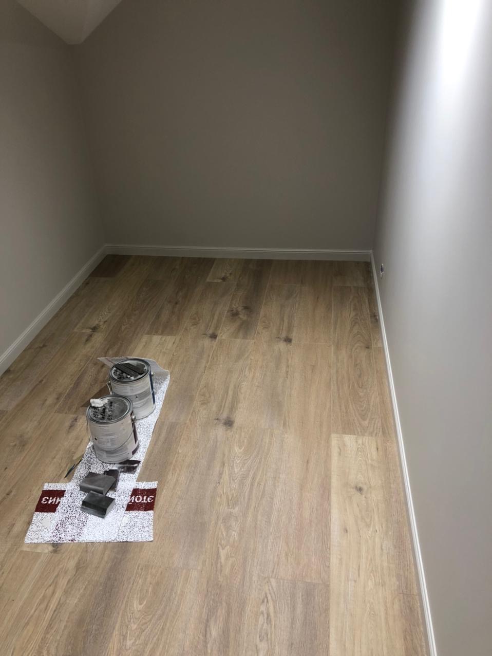 Pomalowane na szaro wnętrze z drewnianą podłogą. Na podłodze pędzle i dwie puszki z farbą na folii ochronnej. Świeżo po malowaniu.