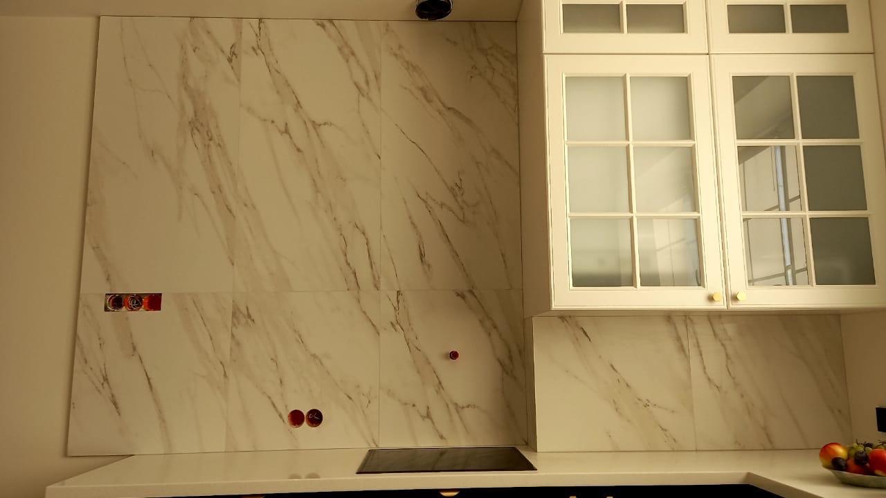 Wykończona ściana w kuchni z marmurowymi płytkami, widoczne gniazdka elektryczne i szafki wiszące z przeszklonymi drzwiczkami. Nowoczesny design.