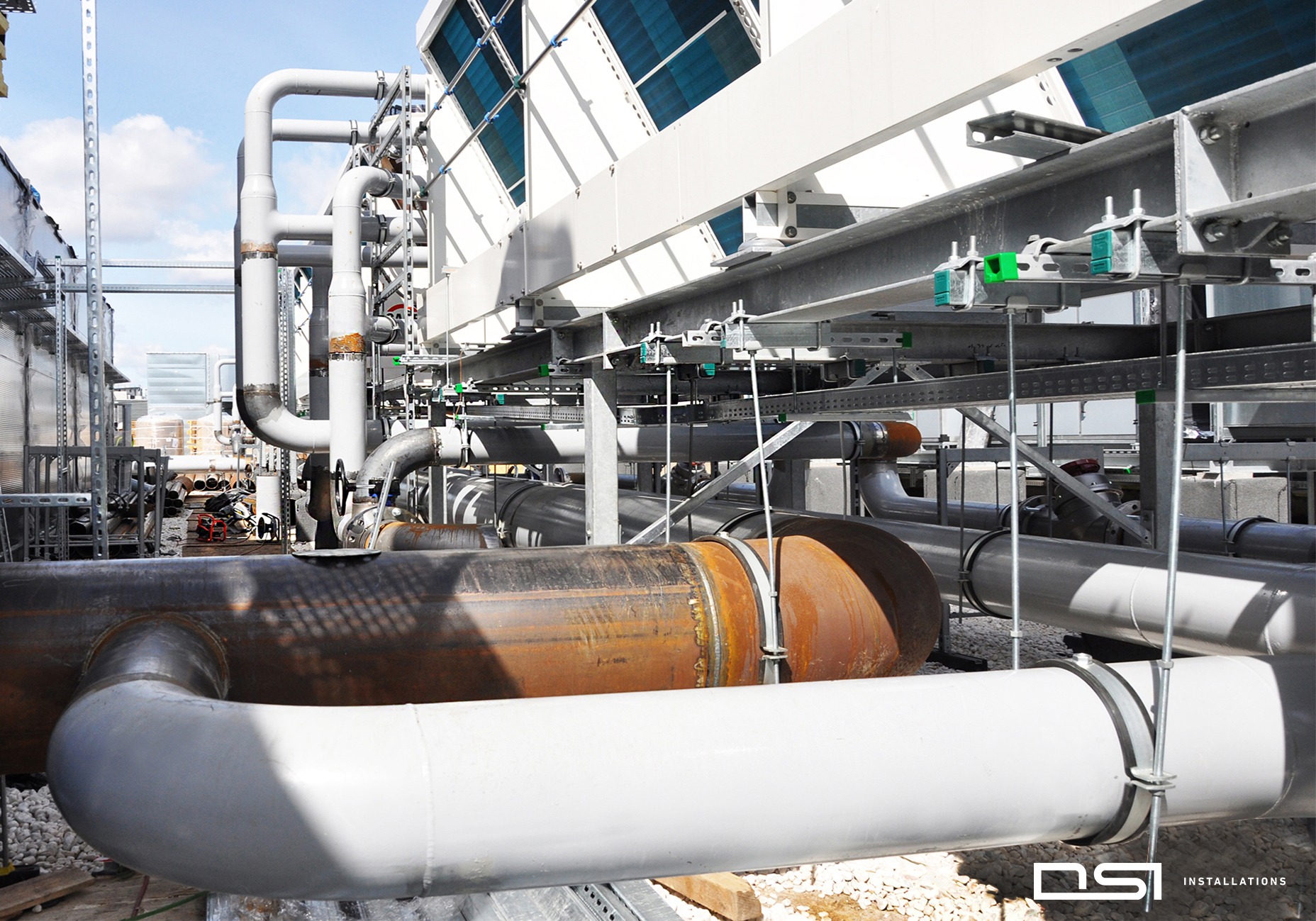 Kompleksowa instalacja przemysłowa z rurami w różnych kolorach i elementami chłodniczymi, zrealizowana w Warszawie. Widoczne mocowania i elementy konstrukcyjne.