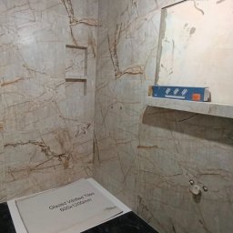REMEXPERT - Wykończona łazienka z marmurowymi płytkami, wnęką i czarnym blatem. Widoczny poziomica i karton z informacją o płytkach. Częściowo odkryta ściana.