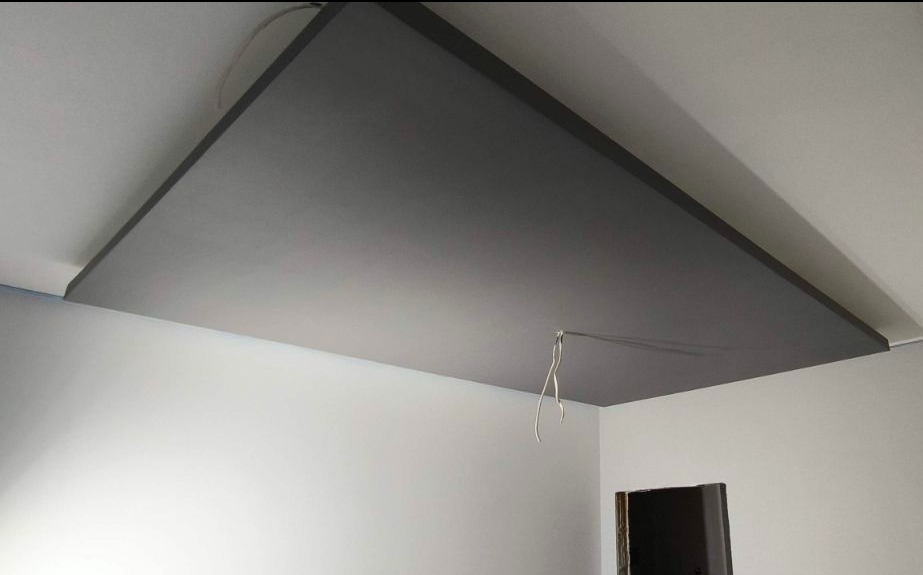 Szary sufit podwieszany z widocznym kablem, zamontowany w rogu białego pomieszczenia. Minimalistyczne wykończenie wnętrza, widok z dołu.