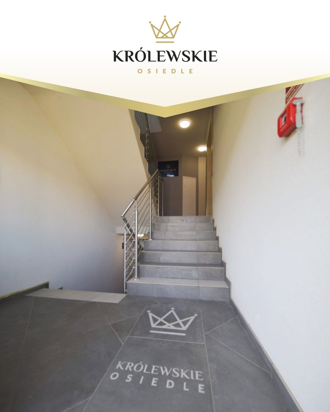 Klatka schodowa z logo osiedla w Stargardzie. Szare płytki na podłodze i schodach, metalowe barierki. Na ścianie czerwona skrzynka przeciwpożarowa.