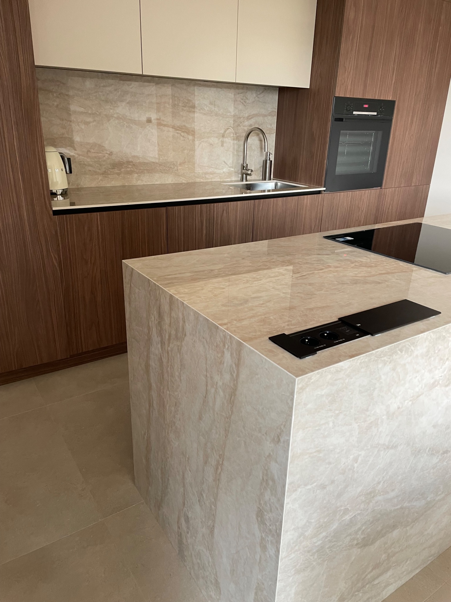 Beżowy blat kuchenny z kamienia z wbudowanym gniazdkiem, dopasowany do ściany nad zlewem i drewnianych szafek. Widoczna płyta indukcyjna i piekarnik.