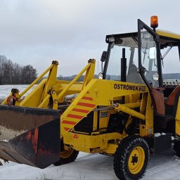 POLMAR Marcin Puchalski - Żółta koparko-ładowarka Ostrowek NK-0352B na zasypanym śniegiem polu. Widoczne ramię koparki, łyżka i kabina. Na maszynie czerwone pasy i oznaczenie 255.