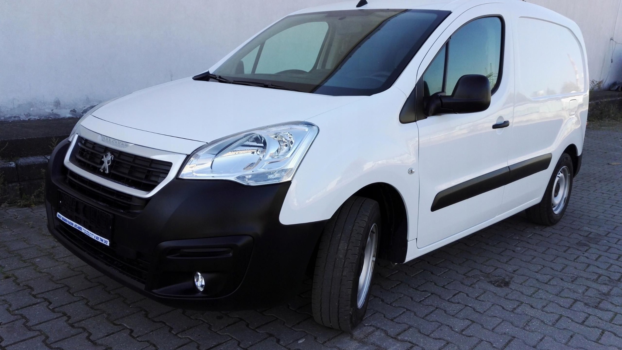 Biały, dostawczy Peugeot Partner z czarnym zderzakiem na kostce brukowej. Widok z przodu, lekko z boku. Auto czyste, zadbane, gotowe do transportu.