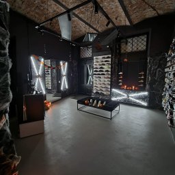 Michał Sikora - Mroczny wystrój sklepu obuwniczego z ceglanym sufitem, halloweenowymi dekoracjami i podświetlonymi półkami pełnymi butów sportowych.