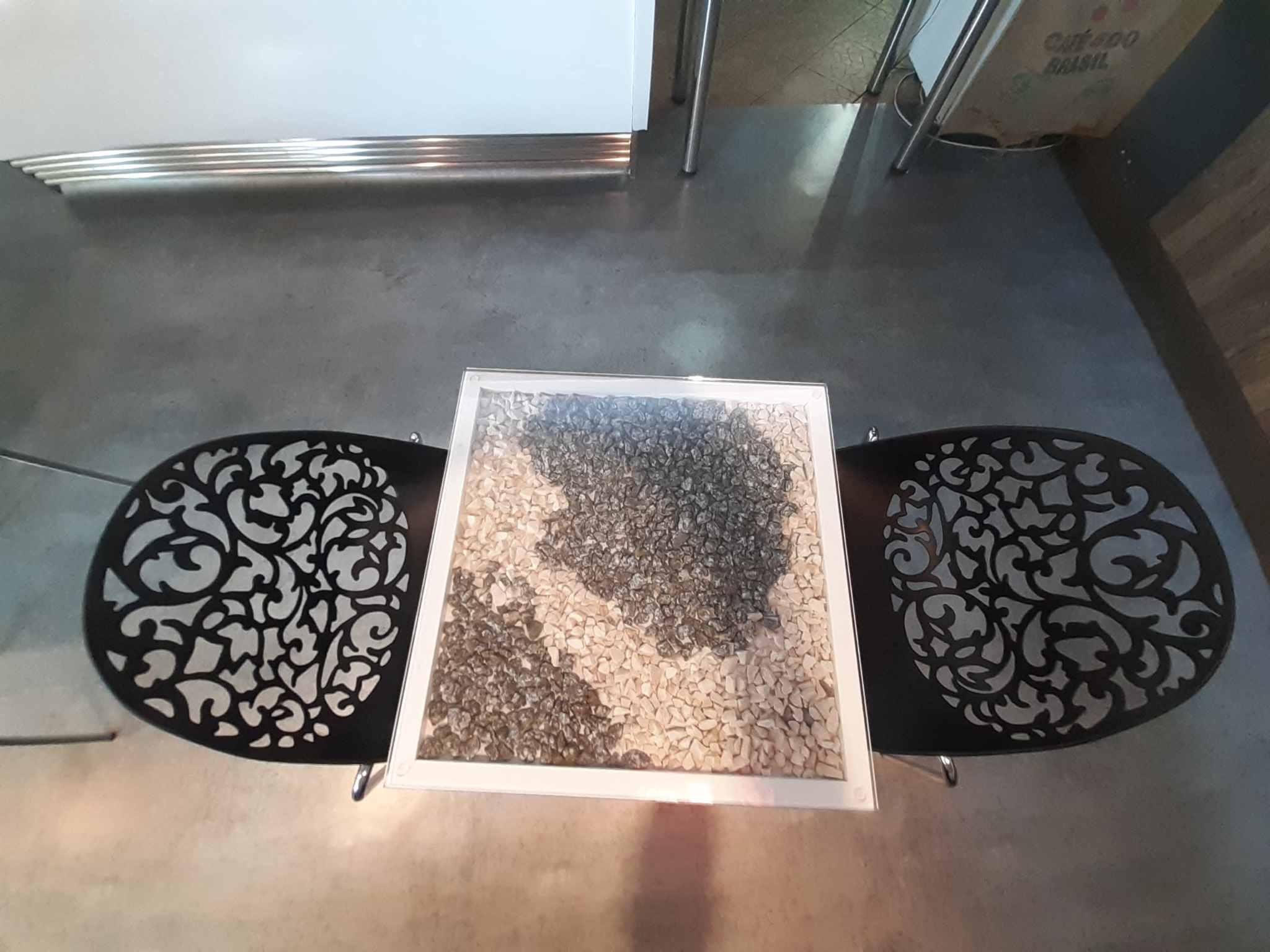 Dekoracyjny stolik kawowy z mozaiką z kamieni, otoczony dwoma krzesłami z ażurowym wzorem, widziany z góry w nowoczesnym wnętrzu.