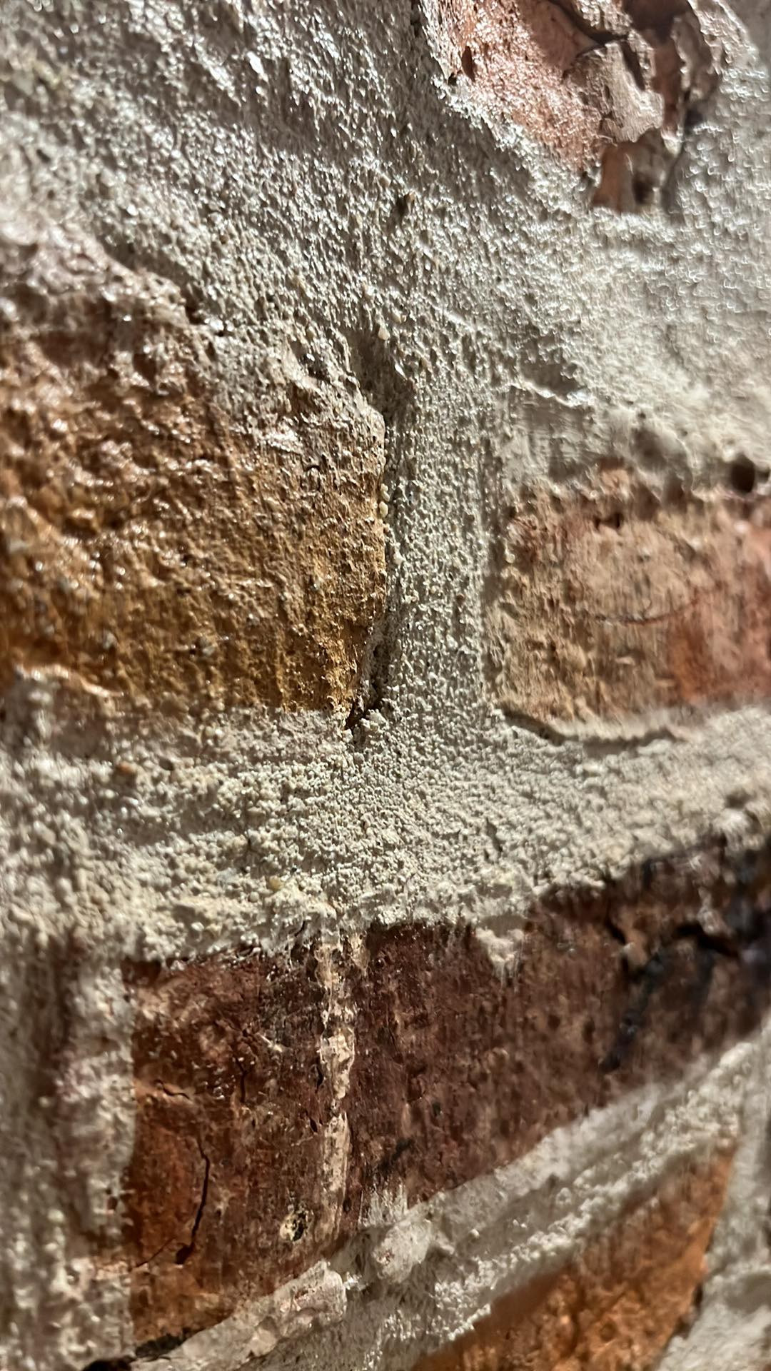 Ceglany mur z grubą warstwą zaprawy, ukazujący fakturę i detale materiałów budowlanych w bliskim ujęciu, z widocznymi nierównościami i chropowatością powierzchni.