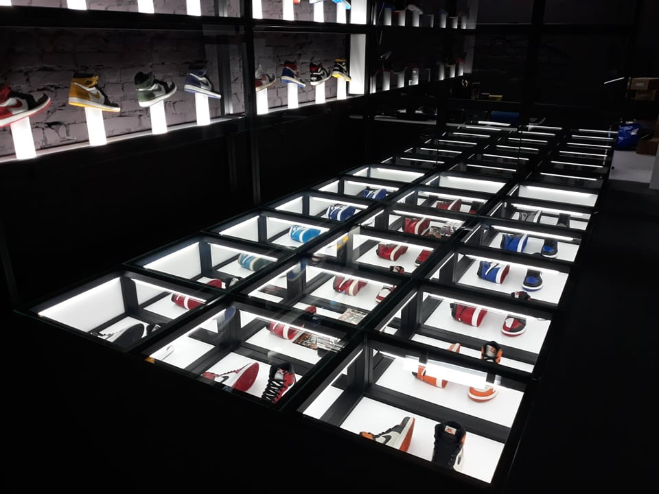 Nowoczesna ekspozycja obuwia sportowego w podświetlanych gablotach podłogowych i na półkach ściennych, tworząca unikalny wystrój wnętrza sklepu.