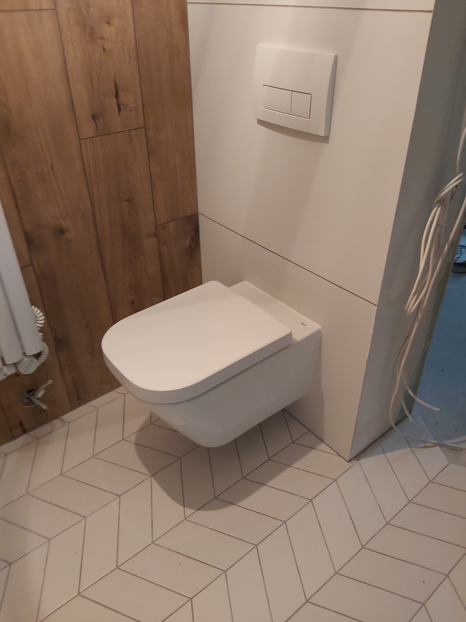 Nowoczesna, podwieszana toaleta w wykończonej łazience. Biała ceramika, drewniane panele ścienne i geometryczne płytki podłogowe tworzą spójny design.