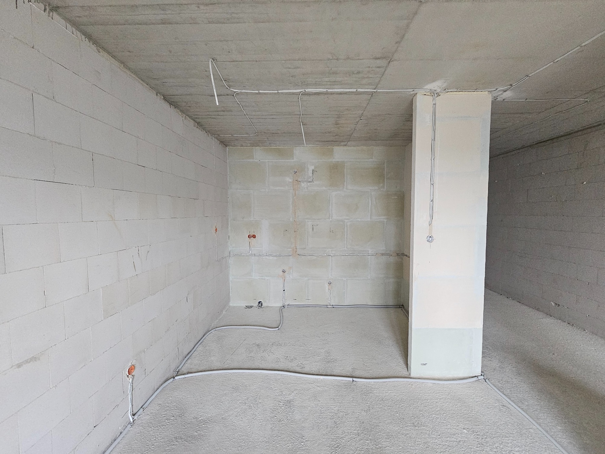 Surowy stan wnętrza z widoczną instalacją elektryczną w peszlach na podłodze i przewodami pod sufitem. Ściany z białego betonu komórkowego, surowy betonowy strop.