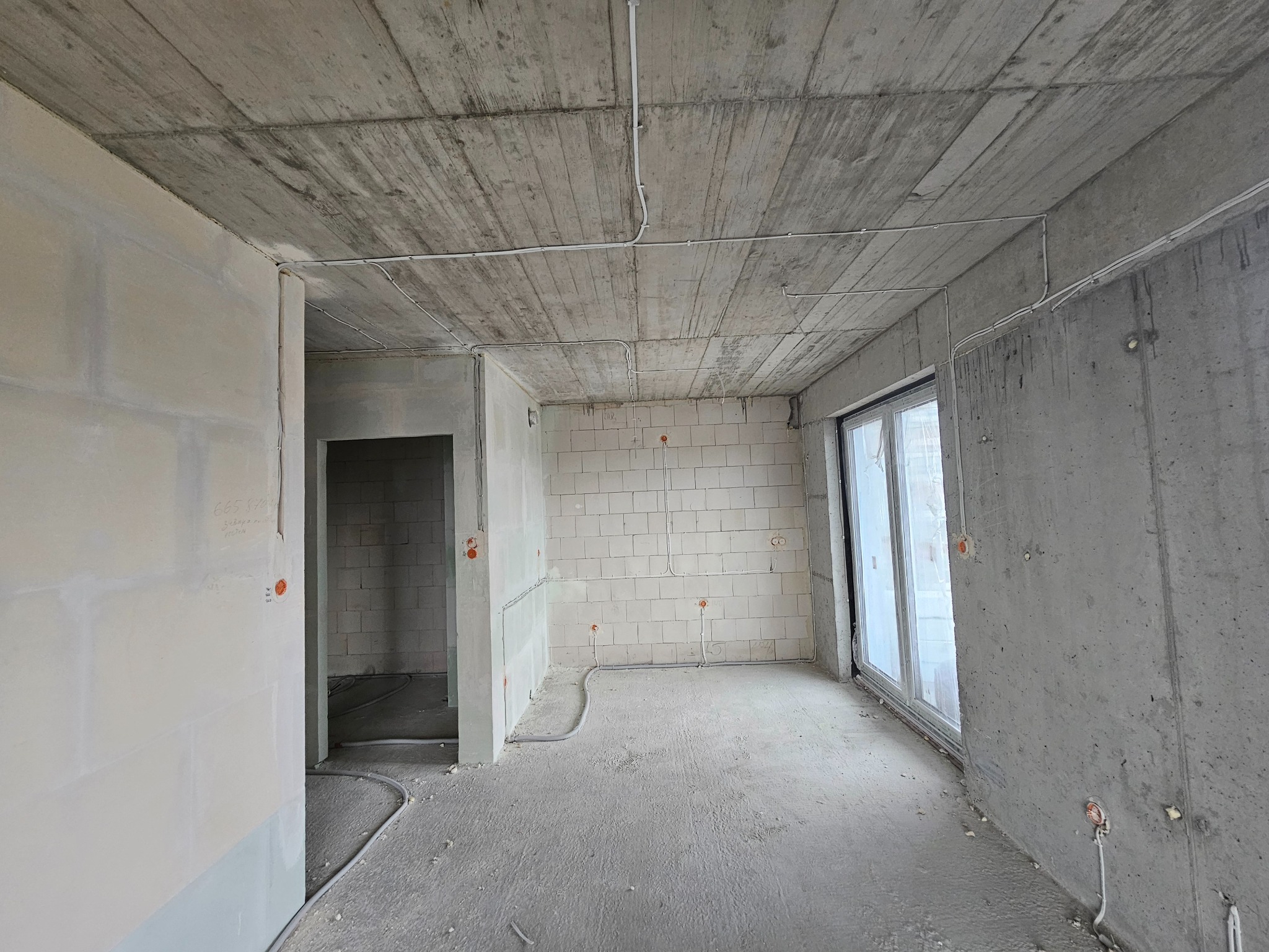 Surowy stan wnętrza: betonowy sufit, ściany z pustaków i gipsu, instalacja elektryczna w peszlach, okno balkonowe. Wnętrze w trakcie prac wykończeniowych.