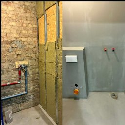 Firma Usługowa ProfesRemont Dominik Baran - Remont łazienki: ściana z cegły przed izolacją i zabudową, oraz wykończona, szara ściana z podtynkową instalacją sanitarną i odpływem. Etapy prac.