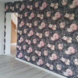 MKiP - Pokój po remoncie: ściana w kwiaty, jasna podłoga, widok na schody. Nowoczesne wykończenie wnętrza z tapetą w stylu vintage i świeżo położonymi panelami podłogowymi.