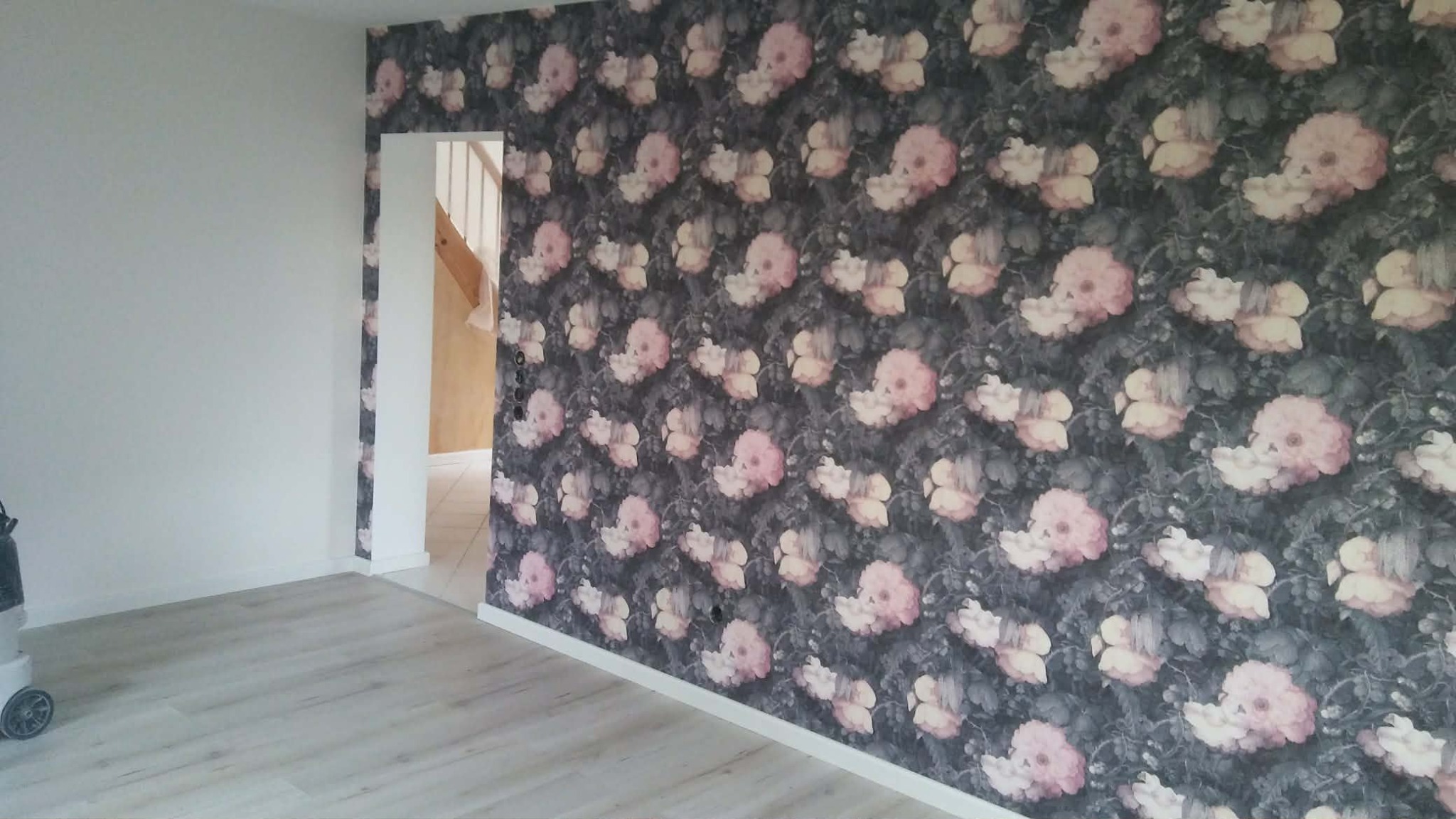 Pokój po remoncie: ściana w kwiaty, jasna podłoga, widok na schody. Nowoczesne wykończenie wnętrza z tapetą w stylu vintage i świeżo położonymi panelami podłogowymi.