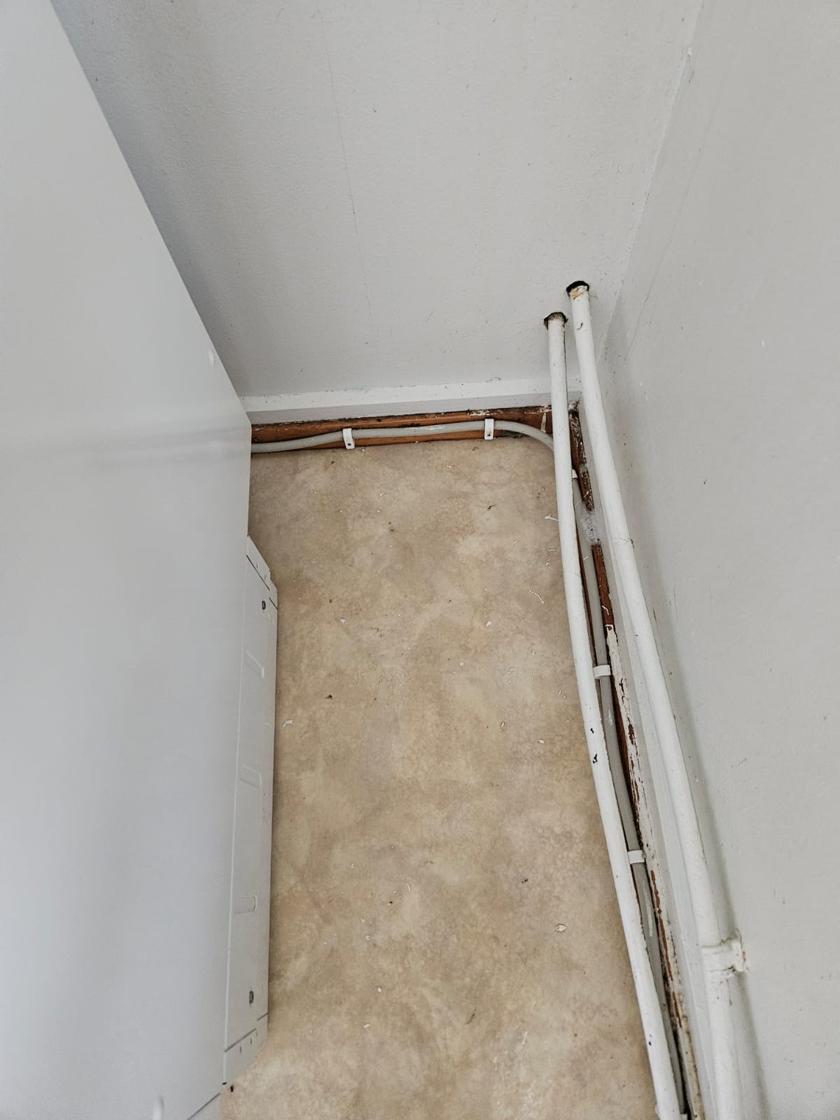 Kątowe ujęcie podłogi i ścian po remoncie, z widocznymi rurami grzewczymi i fragmentem białej szafki. Widoczne ślady po pracach remontowych.
