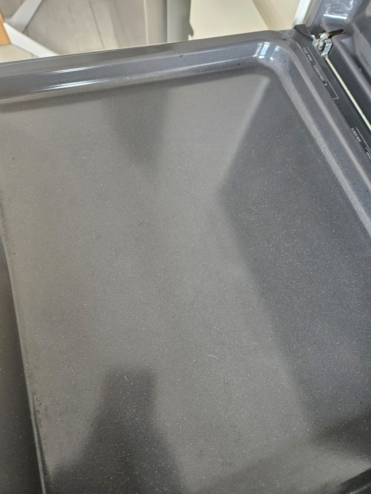 Szary wnętrze piekarnika z widocznymi drobnymi zabrudzeniami, ukazujące potrzebę czyszczenia. Ujęcie z góry, bliskie, z detalami tekstury.