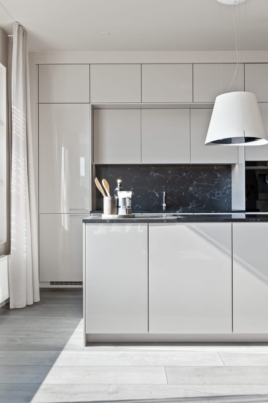 Biała, nowoczesna kuchnia z czarnym blatem i marmurowym panelem. Minimalistyczny design, jasne światło, drewniane przybory kuchenne na blacie. Elegancki wystrój wnętrza.