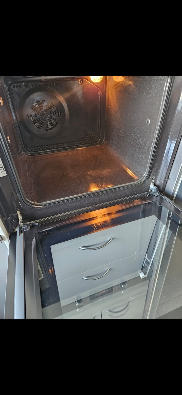 Otwarty piekarnik z widocznymi zabrudzeniami wewnątrz, oświetlony od góry. Widoczna dolna część piekarnika z szufladami. Perspektywa z góry.