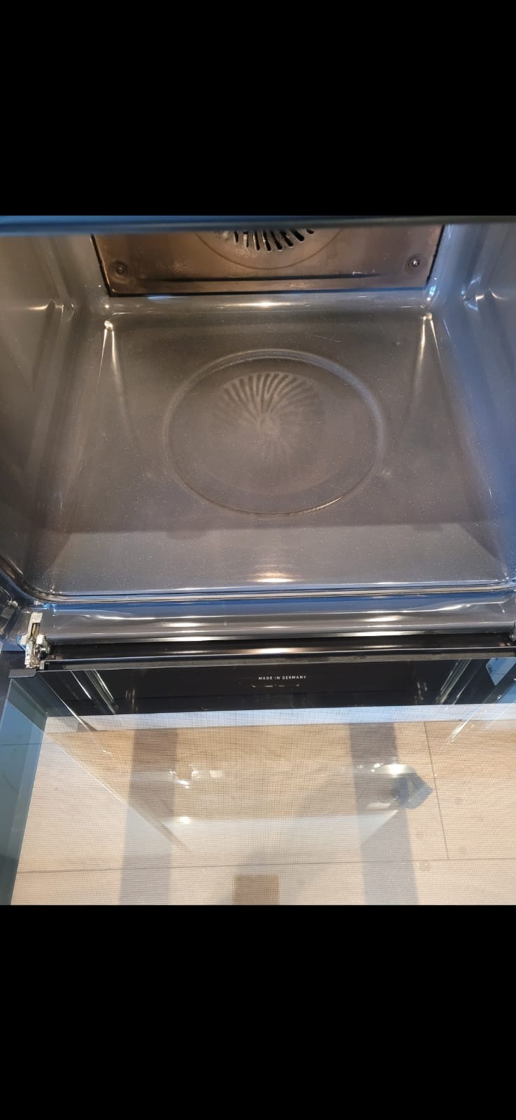 Wnętrze piekarnika z widocznymi śladami użytkowania na dnie i ściankach. Widoczny element grzewczy na górze. Drzwiczki piekarnika uchylone, widoczna podłoga.