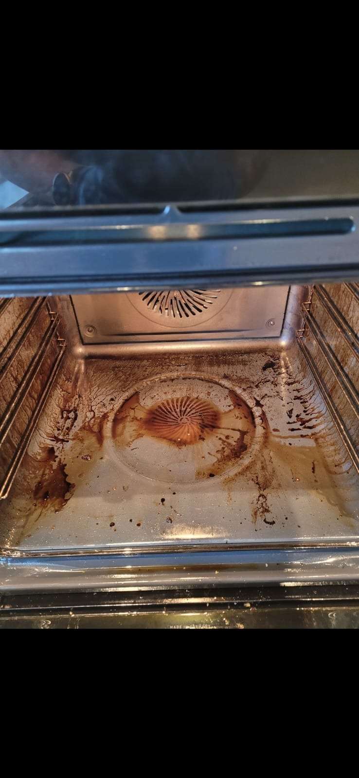 Zanieczyszczone wnętrze piekarnika z przypalonym tłuszczem i resztkami jedzenia na dnie i ściankach. Widoczny element grzewczy. Potrzeba gruntownego czyszczenia.