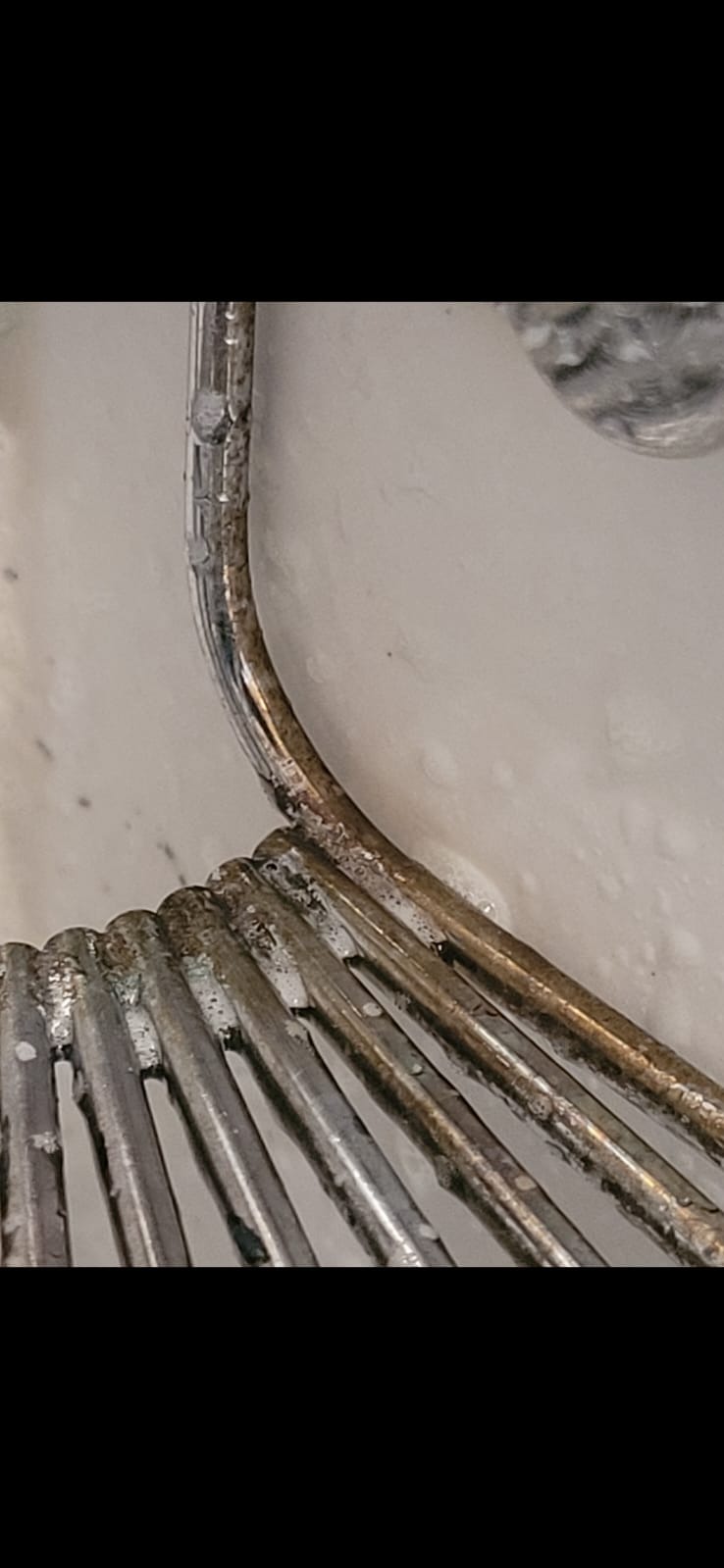 Zbliżenie na metalową trzepaczkę pokrytą zaschniętym brudem i resztkami jedzenia, zanurzoną w mętnej wodzie. Widoczne ślady korozji i niedokładnego umycia.