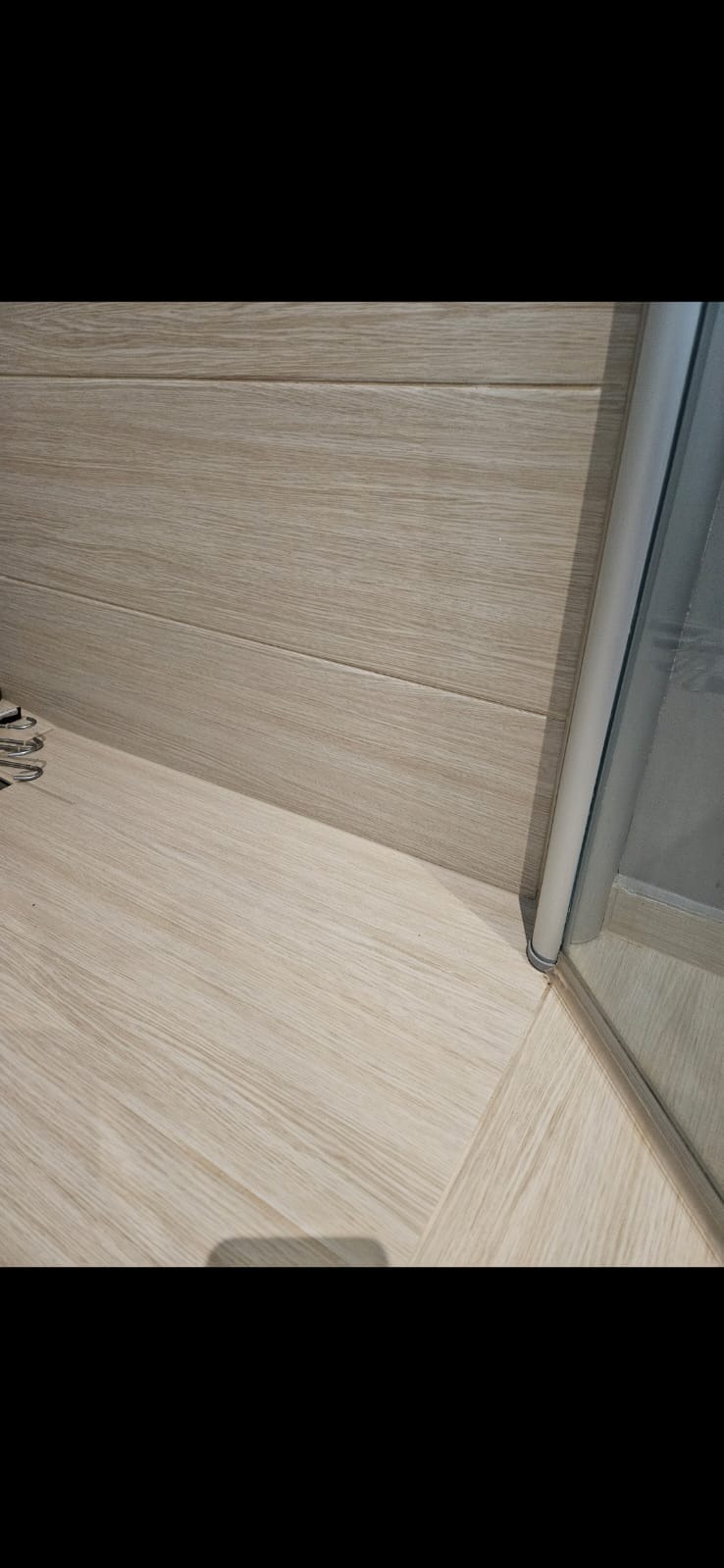 Jasna, drewnopodobna podłoga i ściana w łazience, z fragmentem kabiny prysznicowej. Widoczne detale wykończenia i połączenie materiałów.