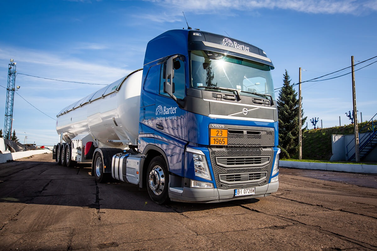 Ciężarówka cysterna firmy Barter w niebiesko-białych barwach, zaparkowana na betonowym placu, z widoczną tablicą ostrzegawczą i logotypem firmy.