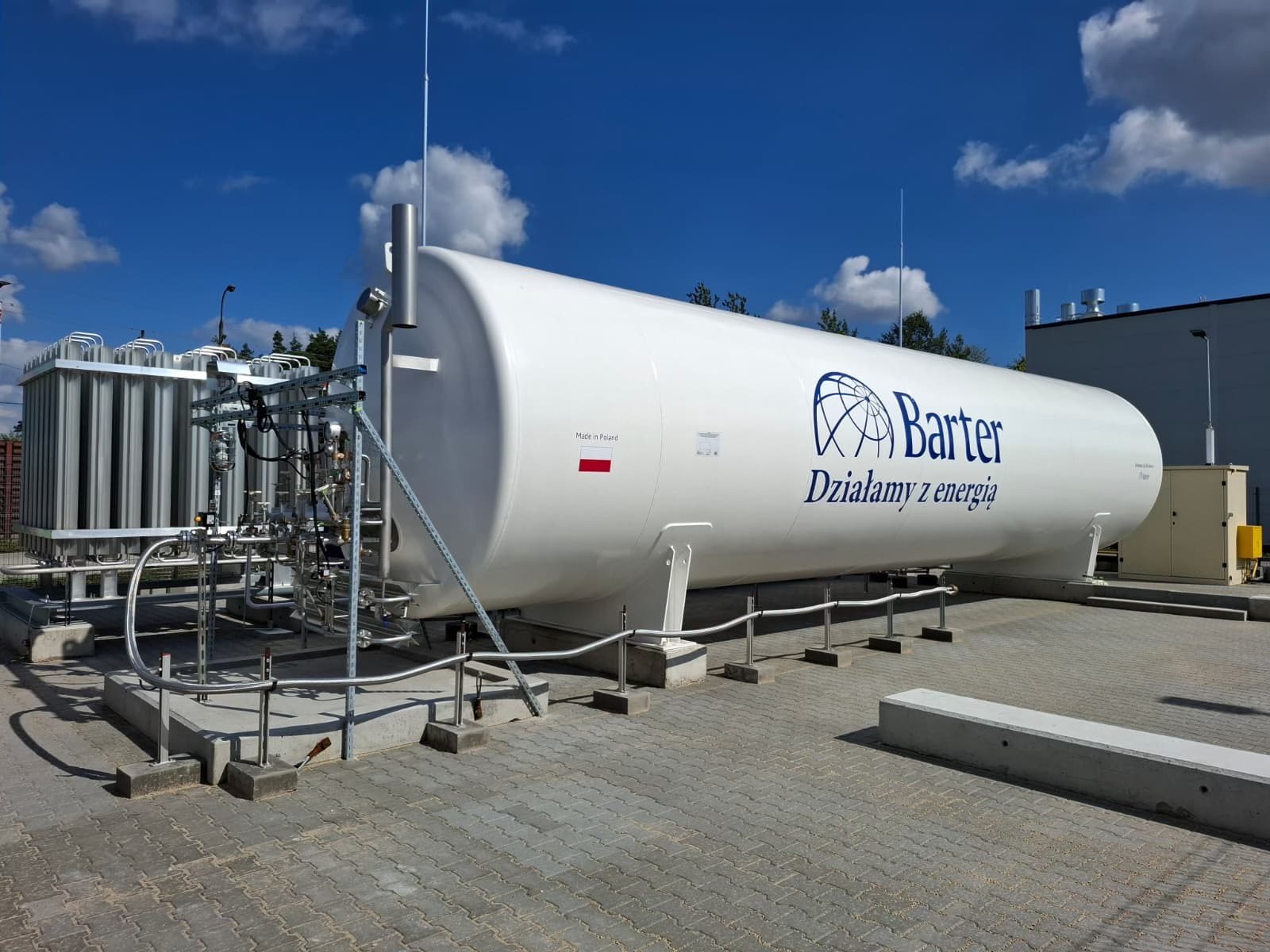 Zbiornik na gaz z logo firmy Barter z Białegostoku, instalacja gazowa, błękitne niebo. Widok na zewnątrz, kostka brukowa.