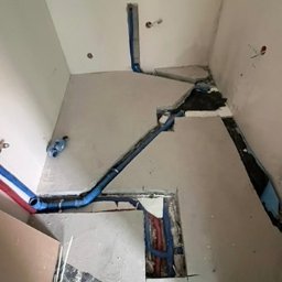 Modena Design - Niebieskie rury instalacji wodnej w bruzdach ścian i podłogi łazienki w trakcie remontu. Widoczne fragmenty ścian i podłogi w surowym stanie.
