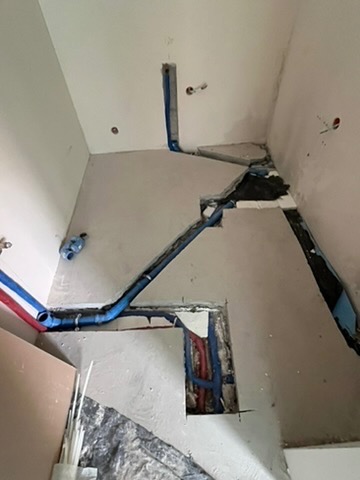 Niebieskie rury instalacji wodnej w bruzdach ścian i podłogi łazienki w trakcie remontu. Widoczne fragmenty ścian i podłogi w surowym stanie.