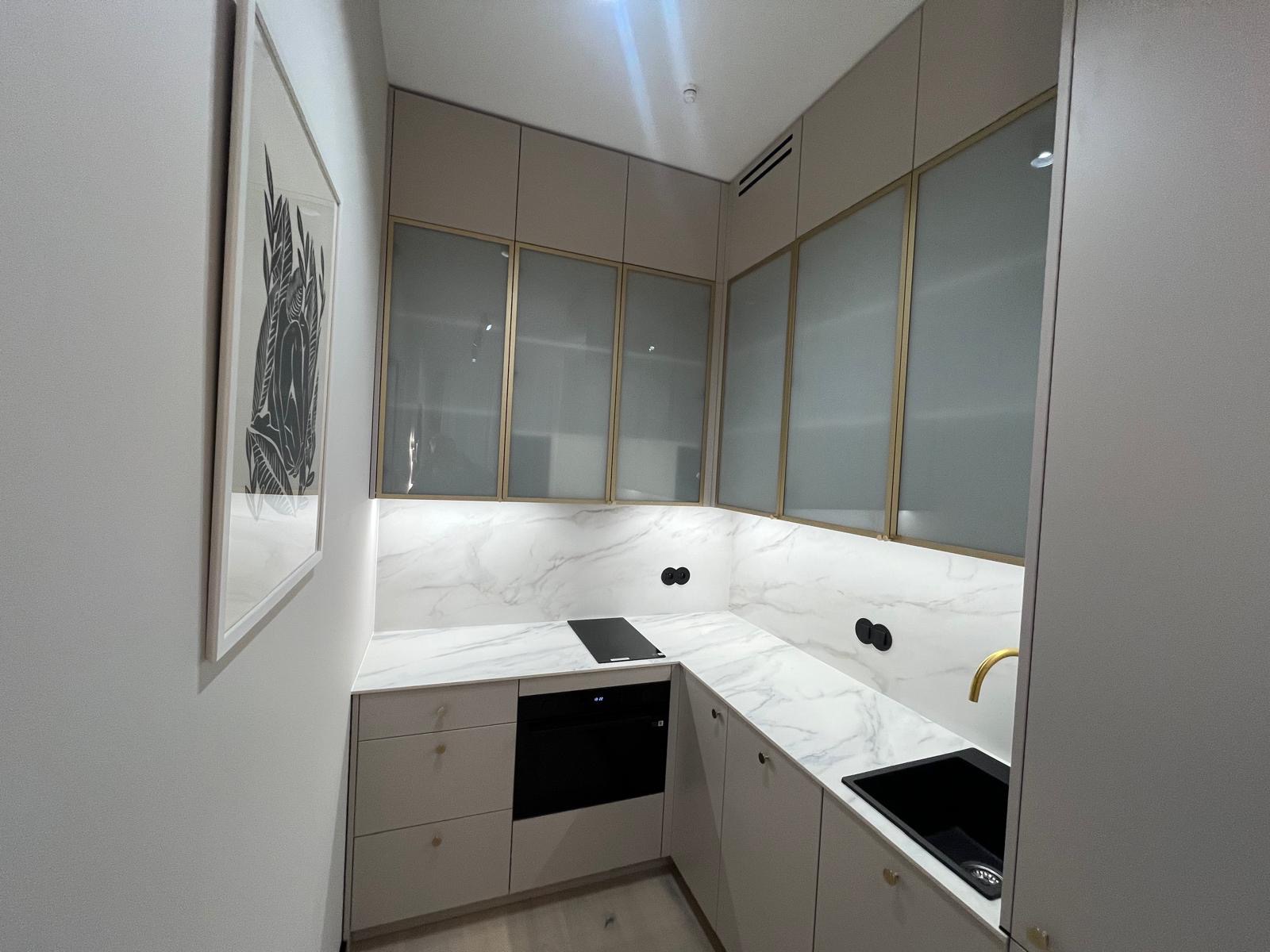 Nowoczesna kuchnia w odcieniach szarości z marmurowym blatem i złotymi akcentami. Na ścianie grafika w białej ramie. Minimalistyczny design, oświetlenie LED.