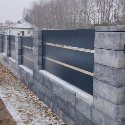 Metalnova - Nowoczesne ogrodzenie z szarego kamienia i paneli w kolorze antracytu, widoczne z perspektywy bocznej na tle zimowego krajobrazu.
