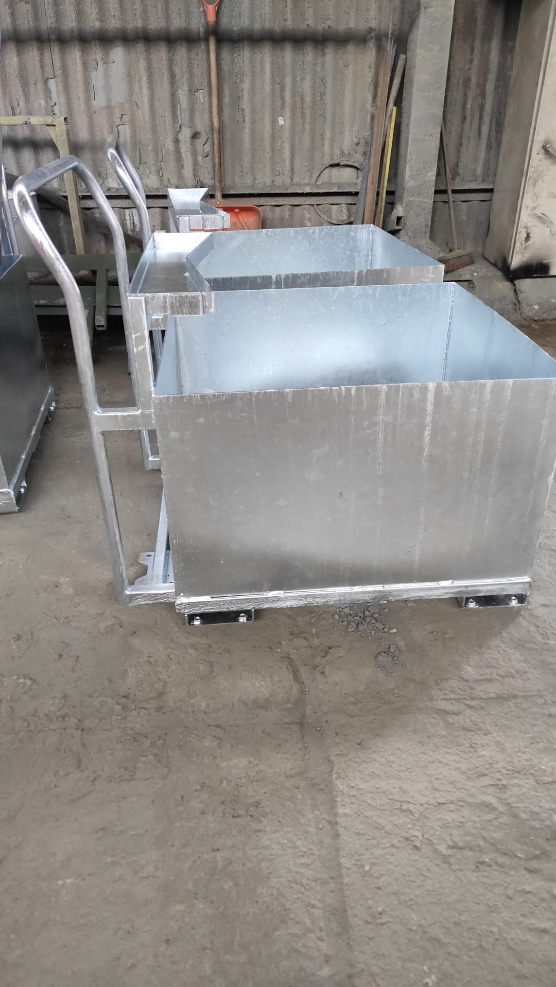 Metalowe wózki transportowe z uchwytami, wykonane z blachy ocynkowanej, ustawione w hali produkcyjnej. Widoczne spawy i elementy mocujące.