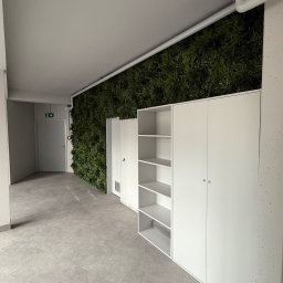 Stolarstwo - Białe szafy wnękowe z półkami, wkomponowane w ścianę z zielenią w Grodzisku Mazowieckim. Minimalistyczny design, jasne wnętrze, nowoczesne rozwiązanie do przechowywania.