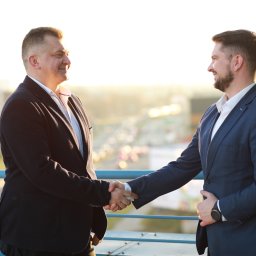 SZAŁAŃSKI I PARTNERZY KANCELARIA RESTRUKTURYZACYJNA SPÓŁKA Z OGRANICZONĄ ODPOWIEDZIALNOŚCIĄ - Uścisk dłoni dwóch mężczyzn w garniturach na tle panoramy Warszawy. Symbolizuje zawarcie umowy, partnerstwo biznesowe, zaufanie i profesjonalizm.