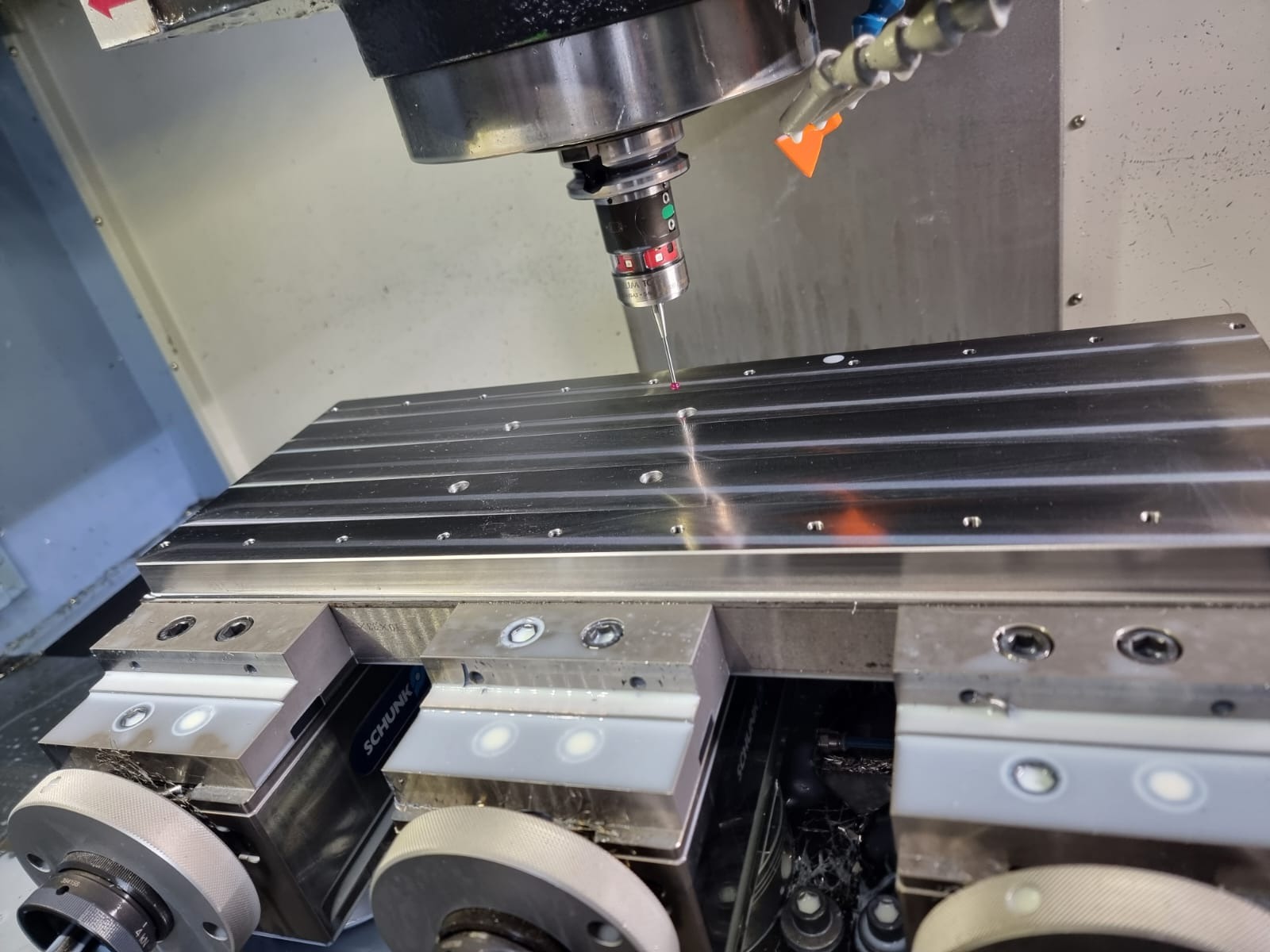 Precyzyjny pomiar detalu na maszynie CNC w Lulinku. Sonda pomiarowa dotyka obrabianego elementu. Widoczne mocowania Schunk i chłodziwo.