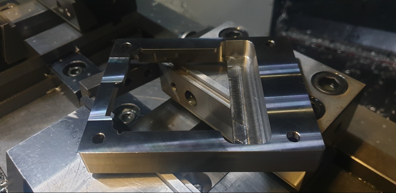 Precyzyjnie obrobiony, metalowy element z widocznymi śladami frezowania, umieszczony na metalowej powierzchni. Detal z otworem i fazowaniem, w otoczeniu wiórów.